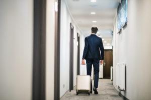Businessman walking with luggage in a hotel corridor.
